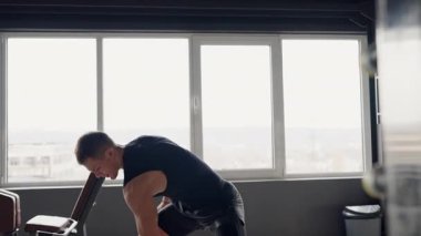 Kararlı genç bir erkek atlet halter egzersizini iyi donanımlı bir spor salonunda yapıyor, gücünü ve dikkatini gösteriyor. Modern Spor Salonunda Ağırlık Kaldıran Genç Adam Ortamı