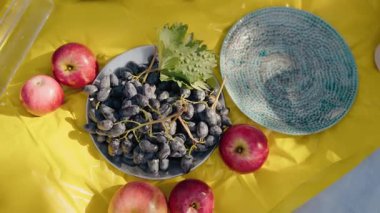 Güneşli bir günde taze elma ve üzümlerin yer aldığı canlı bir açık hava piknik sahnesi, aile ve arkadaş toplantıları için ideal. Taze elma ve üzümlerle güneşli açık hava pikniği
