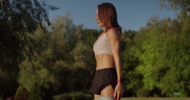 Atletik kadın spor yapıyor ve dışarıda fitness direnci bandıyla çömelme egzersizi yapıyor. Zayıf vücutlu genç bir kadın spor yapıyor ve dışarıda direniş bandıyla takılıyor..