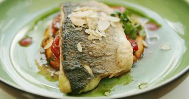 Patates püresi ve sebzeli güzel dekore edilmiş beyaz balık parçası yeşil tabakta ve beyaz arka planda dönüyor. Soslu levrek. Restoran ana yemek konsepti..