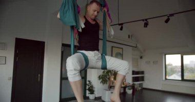 Hafif stüdyodaki yoga seansı sırasında havadan hamakta baş aşağı asılı güçlü bir erkek resmi. Sınıfta çalışıyor, aero yoga yapıyor..