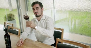 Kırmızı şarabı bardakla karıştıran pozitif şarap garsonu tatma töreninde renkleri değerlendiriyor. Camların dönüşü şarabın yüzeyini dalgalandırıyor ve uzun cam duvarlar boyunca uzanıyor..