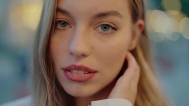 Sarışın ve yeşil gözlü genç bir kadının yakın plan portresi. Bokeh ışıkları olan bulanık bir şehir arka planına kurulmuş. Görüntü güven ve sükunet yayar. Genç Bir Kadının Yakın Çekim Portresi