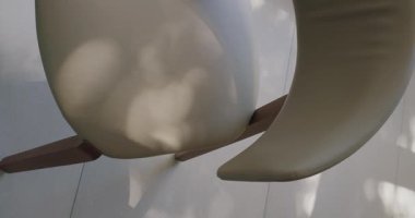 Görünür gölgeli bej bir sandalyenin yansıtıcı mermer zeminde olduğu çağdaş iç mimari bir detay. Minimalist tasarım temaları için ideal. Modern Bej Sandalye Manzarası. Dikey video.