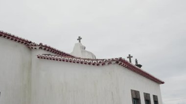 Portekiz 'de kırmızı kiremitli çatıları ve birden fazla haçı olan eski bir beyaz kilise binası, dinginlik ve maneviyat taşıyor. Portekiz 'in çatısında haçlar olan tarihi kilise binası.