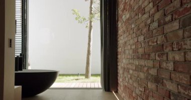 Zarif ve rahatlatıcı bir iç mekan modern bir küvet ve çarpıcı tuğla bir duvar, sakin bir bahçe manzarası ve pencereden ağaçlarla çevrili. Tuğla Duvar ve Bahçe Görünümlü Modern Ev İçi