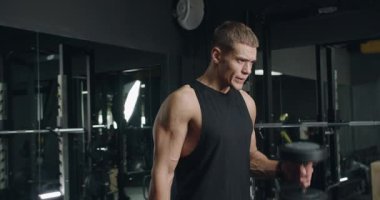 Odaklanmış genç bir adam, iyi donanımlı bir spor salonunda dambılları kaldırıyor, güç antrenmanı ve yoğun egzersiz rutinini gösteriyor. Modern Spor Salonunda Ağırlık Kaldıran Genç Adam