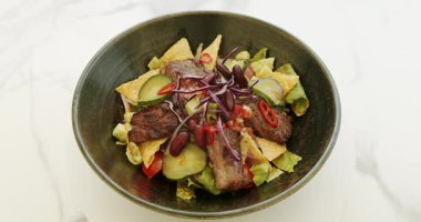 Etli salata, fasulye, vişneli domates, salatalık, kırmızı biber, kırmızı soğan, lahana salatası, beyaz arka planda dönen büyük tabakta nachos cipsi. Taco salatası. Lahana ve fasulye salatası..