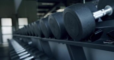 İyi ışıklandırılmış modern bir spor salonunun rafına yerleştirilmiş ağır siyah halterlerin yakın plan görüntüsü fitness ve kuvvet eğitiminin göstergesidir. Modern Spor Salonunda Ağır Dambıllar Sırası