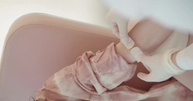 Eldivenli bir sağlık uzmanı, hafif ışıklandırılmış bir klinik ortamında hastanın bileğine bandaj sarar. Klinikteki Hastalara Bandaj Uygulayan Profesyonel Bakıcı