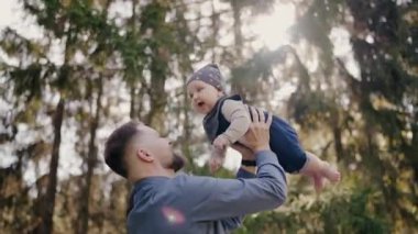 Genç bir aile dışarıda mutlu bir anın tadını çıkarırken ebeveynler, yavrularını ormanla çevrili bir şekilde mutlulukla havaya kaldırıyorlar. Ormandaki Neşeli Aile Anı: Ebeveynler Bebeği Gülümseyerek Kaldırıyor