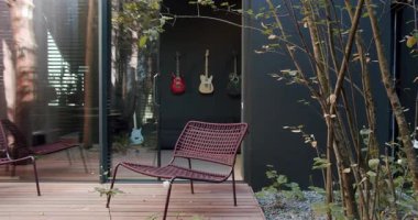 Çağdaş bahçe verandasında, doğa ve müzik dekorunu zarif bir şekilde harmanlayan, üç gitarlı şık koltuklar sergileniyor. Mobilyalı Mobilyalı ve Asılı Gitarlı Modern Ev Harici