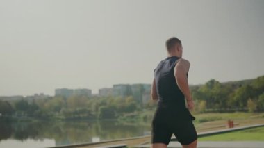 Genç bir adam, çevresi şehirli ağaçlarla çevrili sakin bir göle bakıyor. Bir anlık tefekkür ve doğada huzur. Şehir Parkı 'nda Göle Bakan Genç Adam