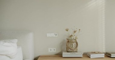 Rahat bir yatak odası, ahşap bir komodin, kitaplar, cam bir vazoda kurumuş çiçekler ve rahat ve rahatlatıcı bir atmosfer yaratan yumuşak bir pencere ışığı..