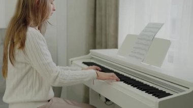 Genç kız evde piyano çalışıyor. Eğitim ve öğrenim geliştirme konsepti. Odaklanmış genç, güzel bir kız. Elektrikli piyano çalarak eğleniyor. Piyano öğrenme dersleri