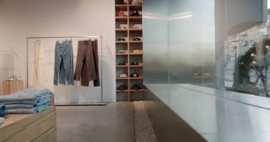 Moda kıyafetleri olan modern şehir giyim mağazası. Minimalist tasarım, şapkalı ve şapkalı ahşap raflar, pantolonlu elbise askılığı, beton zemin, vitrin manzarası. Şık ve modaya uygun butik.