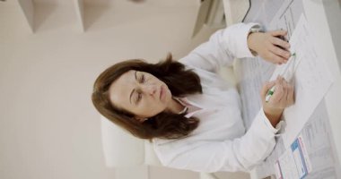 Profesyonel bir kadın doktor, tıbbi belgeleri titizlikle incelerken, sağlık hizmetlerine odaklanma ve adanmışlık gösteriyor. Klinikteki Doktor Reviewing Tıbbi Kayıtları. Dikey video.