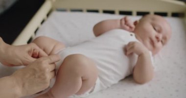 Bebek yatağında bebek bezi değiştiren bir annenin görüntüsü. Sevgi dolu anne yeni doğmuş bebeğiyle ilgileniyor. Annelik kavramı. Genç anne bez değiştirip bebekle oynuyor..