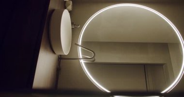 Yuvarlak ışıklı ayna ve minimalist lavabonun yer aldığı çağdaş bir banyo. Parlak ve modern bir iç tasarım sergiliyor. Ev dekorasyonu için mükemmel. Dairesel aynalı modern banyo.