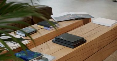 Modern bir iç mekanda, ahşap bir masa üzerinde kitaplar ve dergiler. Okumak ve dinlenmek için rahat bir ortam. Doğal ışık ve şık tasarım rahat bir alan yaratır..