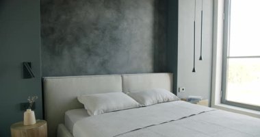 Gri duvarlı, yumuşak tekstil ve minimalist dekorlu modern yatak odası iç tasarımı. Doğal ışık pencereden akar, rahat ve davetkar bir atmosfer yaratır. Rahatlama ve dinlenme.