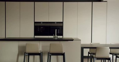 Parlak, bej dolaplı minimalist tasarımı olan çağdaş bir mutfak ve şık sandalyeli merkez bir ada. Modern ev dekorasyonu için mükemmel. Modern Mutfak İçi