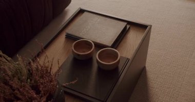 İçinde kitaplar, ahşap kaseler ve dekoratif bitkiler olan şık bir kahve masası olan rahat bir oturma odası. Sıcak, davetkar atmosfer, rahatlatıcı anlar için mükemmel. Modern ev dekorasyonu ilham kaynağı.