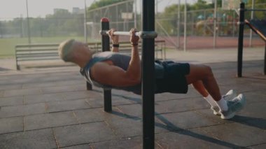 Güneşli bir günde, açık havada vücut ağırlığı egzersizi yapan zinde genç bir adam bir park ortamında kendini adamış ve gücünü gösteriyor. Genç adam güneşli bir günde vücut ağırlığı eğitimiyle dışarıda egzersiz yapıyor.