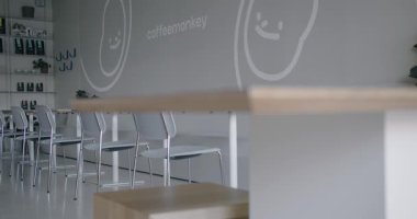 Bu resim, parlak mobilyaları ve nötr renkleri olan temiz, minimalist bir tasarıma sahip modern bir kahve dükkanı sergiliyor. Mekan aydınlık ve davetkar.