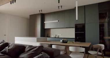 Modern açık mutfak ve oturma odası iç mimarisi. Rahat bir kanepe, doğal ahşap yemek masası ve sandalyeler, şık lambalar ve şık mutfak dolapları. Minimalist, ferah ve davetkar..