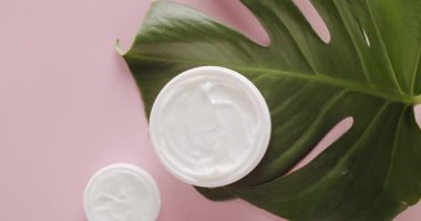 Stüdyoda pembe arka planda tropikal yapraklı Kozmetik için beyaz kavanozlar. Kremalı parlak kozmetik kavanozlar. Güzellik tedavisi için Monstera yapraklı şişe kremleri. Doğal.