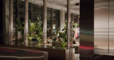 Geceleri Fabrikalarla Modern Yönetim Kurulu İçişleri. Giysi rafları olan boş bir galeri. Yeşil bitkileri ve rahat koltukları olan şık bir iç dizayn. Şehir ortamında moda mağazası.