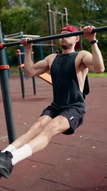 Kararlı bir adam, açık hava spor salonunda barfiks çekiyor. Sağlıklı ve aktif bir yaşam tarzına olan bağlılığını ve gücünü göstermek için spor rutinine odaklanıyor..