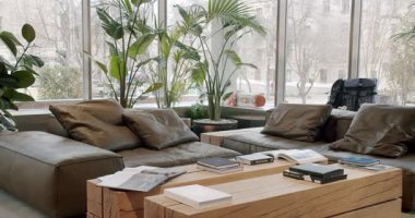 Deri koltuklar, ahşap masalar, dergiler ve ev bitkileriyle modern pano mağazası. Büyük pencereler doğal ışık ve şehir caddesi manzarası sunuyor.