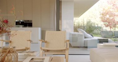 İki hasır sandalye ve bir sehpası olan modern, minimalist bir oturma odası. Verandaya beyaz kanepeli büyük cam kapılar açılıyor. Arka planda beyaz dolaplı mutfak görünüyor..