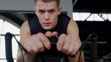 Yoğun odaklı genç bir adam spor salonunda bir fitness makinesi kullanıyor, azim ve güç gösterisi yapıyor. Spor Salonu Spor Makinesi 'ne Yoğun Odaklanmış Genç Adam Eğitimi