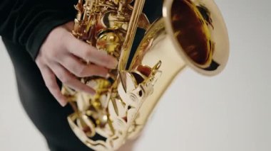 Siyah elbiseli genç bir kadın stüdyoda beyaz arka planda saksafon çalıyor. Romantik müzik. Saksafon çalan genç bir bayan müzisyen. Saksafon çalan caz müzisyeni..