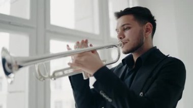 Modern bir stüdyonun penceresinin yanında trompet çalan bir erkek caz şarkıcısı. Canlı caz konseri. Müzik tutkusu. Genç trompetçinin yakın eli. Müzik odası.