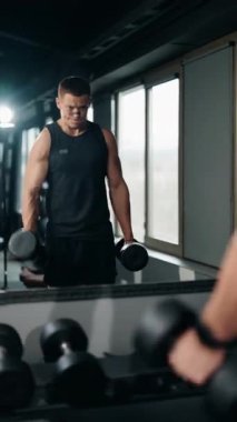 Kas yığını bir adam spor salonunda aynanın önünde dambılları kaldırır. O, pazıları üzerinde çalışırken odaklanmış ve kararlıdır. Sıkı çalışıyor ve kaslarını geliştirmeye çalışıyor..