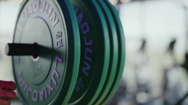 Spor salonundaki bir halterin ağırlığına ağırlık ekleyen birinin elini kapat. Ağırlıklar mor harflerle yeşildir. Siyah bir bilezik takıyor..