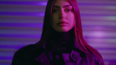 Uzun kahverengi saçlı genç kadın model renkli arka planda poz veriyor. Şatafatlı ve seksi bir kadın gece vakti dışarıda renkli bir arka planda kameraya bakıyor. Güzel kız kameraya bakıyor..