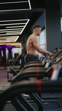 Spor salonunda kaslı bir adam koşu bandında koşuyor. Antrenmanına odaklanmış. Spor salonu modern ve iyi donanımlıdır. Sağlık, zindelik ve kararlılık, yaşam tarzı ve sağlık projeleri.