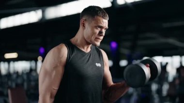 Kararlı bir erkek sporcu modern bir spor salonunda dambılları kaldırır. Egzersizine odaklanıyor ve güç kazanıyor. Egzersiz, spor, kaslar ve spor aletleri aktif yaşam tarzını geliştirir. fitness, spor,