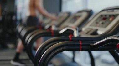 Arka planda egzersiz yapan bir kişinin bulanık figürünün olduğu modern bir spor salonunda koşu bandının yakın çekimi. Ekipmanlara odaklan, aktivite ve zindelik hissi yarat. İyilik ve egzersiz..