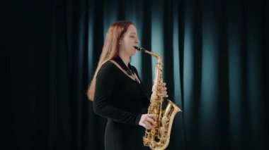 Siyah elbiseli genç bir kadın stüdyoda siyah arka planda saksafon çalıyor. Saksafon çalan caz müzisyeni. Siyah bir gece elbisesi giymiş, sahnede solo yapan bir kadın saksafoncu..