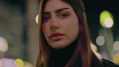 Gece lambalarının arka planında genç bir kadının portresi. Şehir, gece, kız, ışık, dışarıda, güzellik, akşam, kentteki poz verme caddesi. Sokaktaki doğal güzellik kraliçesi. Yavaş çekim.