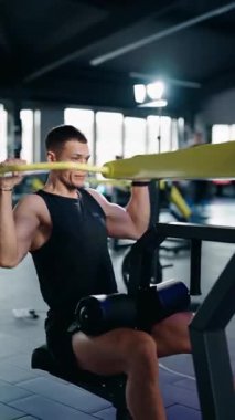 Kaslı bir adam modern bir spor salonunda son çekimleri yapıyor. Formuna ve solunumuna odaklanıyor. Gücünü forma sokuyor. Bu dikey video kararlı bir çalışmanın özünü yakalar.