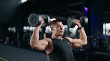 Kararlı bir erkek sporcu modern bir spor salonunda halterli omuz presi yapar. Düzgün forma ve dayanıklılık eğitimine odaklanıyor. Bu video egzersiz için uygunluk, sağlık ve adanmışlığı somutlaştırır..