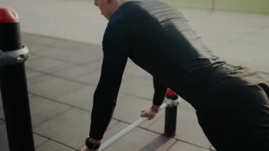 Odaklanmış genç bir erkek modern bir açık hava spor salonunda şınav çeker, şehir ortamında sağlık ve zindelik bağlılığını gösterir..