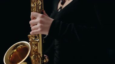 Siyah elbiseli genç bir kadın stüdyoda siyah arka planda saksafon çalıyor. Saksafon çalan caz müzisyeni. Siyah bir gece elbisesi giymiş, sahnede solo yapan bir kadın saksafoncu..